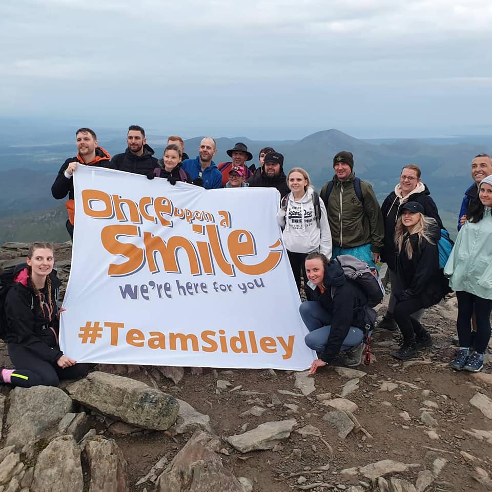A group of people at the top of Snowdon with a OUAS banner